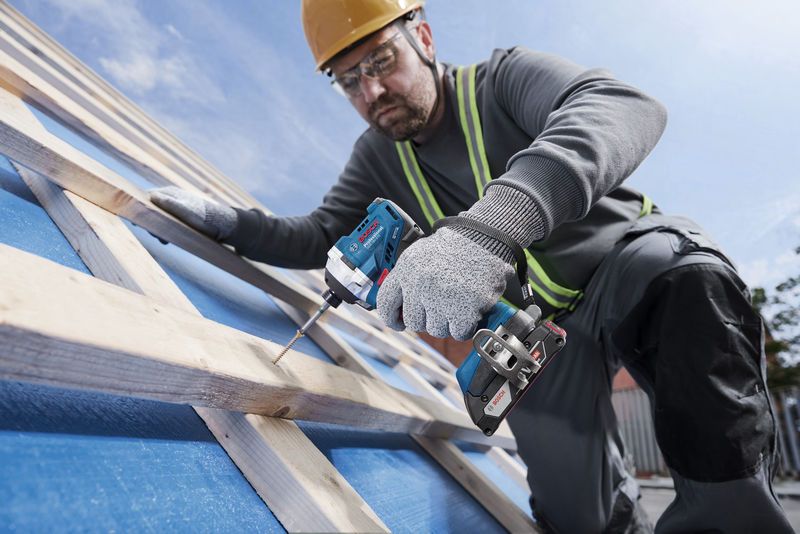 Seseorang yang mengenakan perlengkapan keselamatan menggunakan bor tanpa kabel untuk memasang sekrup pada balok kayu.