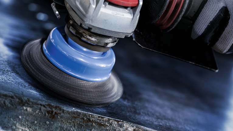 Orang yang mengenakan peralatan keselamatan memoles permukaan logam dengan alat putar.