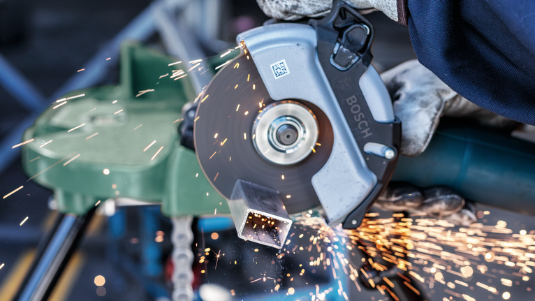 Seseorang yang mengenakan peralatan keselamatan memotong pipa logam dengan penggiling sudut, percikan api beterbangan.