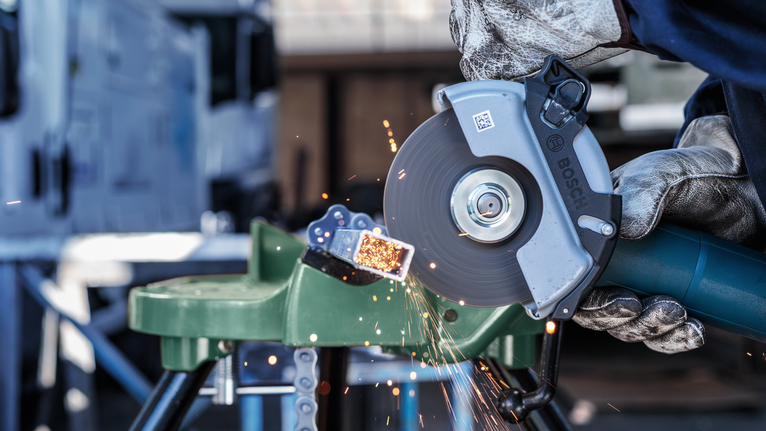 Orang yang mengenakan peralatan keselamatan memotong pipa logam dengan penggiling sudut, percikan api beterbangan.