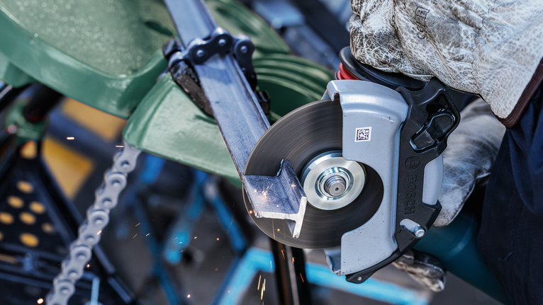 Orang yang mengenakan peralatan keselamatan memotong pipa logam dengan gergaji bundar.