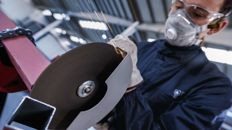 Orang yang mengenakan peralatan keselamatan memotong logam dengan penggiling sudut berputar.