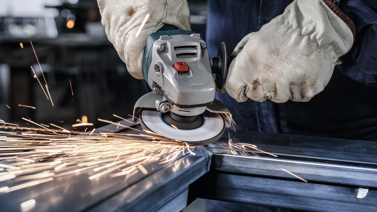 Orang yang mengenakan peralatan keselamatan menggiling logam, menghasilkan percikan terang.