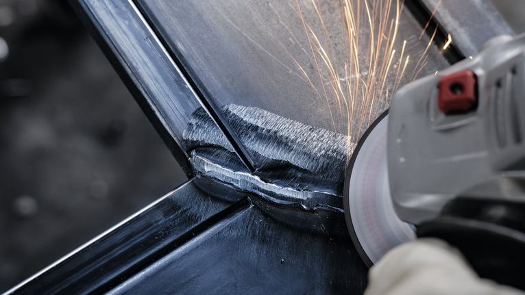 Orang yang mengenakan peralatan keselamatan menggiling las logam, sehingga menimbulkan percikan api.