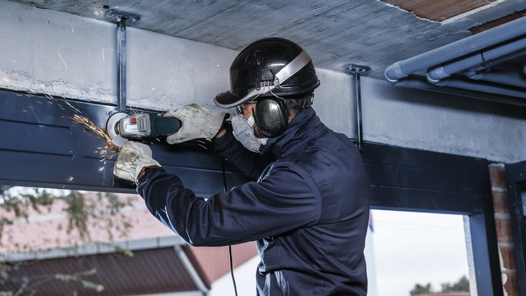 Orang yang mengenakan peralatan keselamatan menggiling balok logam, sehingga menimbulkan percikan api.