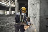 Seseorang yang mengenakan peralatan keselamatan sedang mengasah tulangan beton pada dinding beton dengan penggiling sudut tanpa kabel.