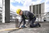 Seseorang yang mengenakan peralatan keselamatan memotong tulangan beton dengan perkakas listrik di lokasi konstruksi.