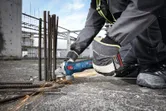 Seseorang yang mengenakan peralatan keselamatan menggiling tulangan beton di lokasi konstruksi, sehingga menimbulkan percikan api.