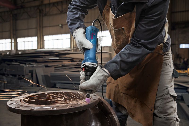 Seseorang yang mengenakan peralatan keselamatan menggiling logam dengan penggiling lurus, menghasilkan percikan api.