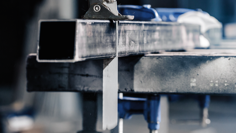 Gergaji logam memotong tabung baja persegi panjang di meja kerja.