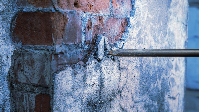 Pahat mengebor batu bata dan beton, menembus permukaan dinding.