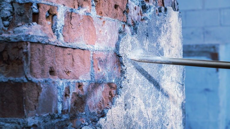 Pahat menghilangkan plester beton dari dinding bata.