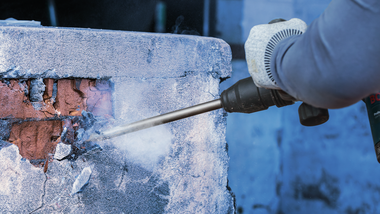 Orang yang mengenakan perlengkapan keselamatan menggunakan alat pembongkaran untuk menghancurkan tembok beton.