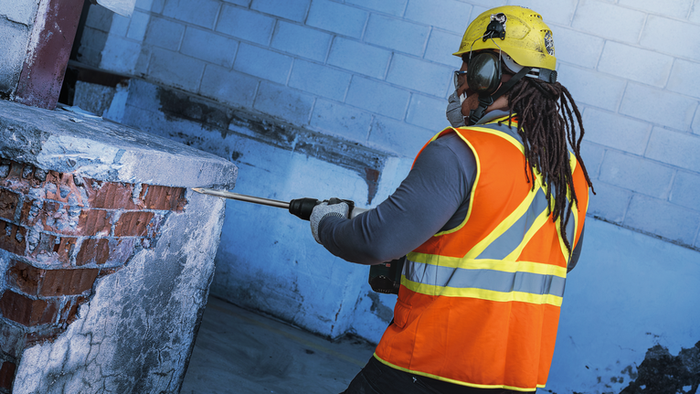 Orang yang mengenakan peralatan keselamatan menggunakan alat pembongkaran untuk memecahkan beton dan batu bata.
