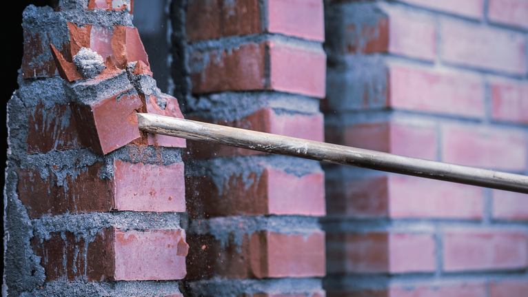Batang penghancur memecah batu bata merah dari dinding mortar.