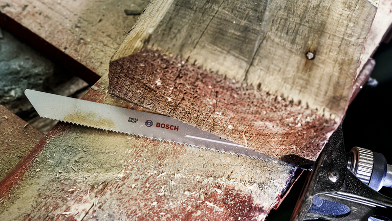 Mata gergaji memotong balok kayu tebal di bengkel.