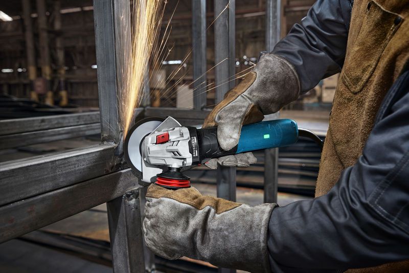 Seseorang yang mengenakan peralatan keselamatan menggiling logam, sehingga menimbulkan percikan api di lingkungan industri.