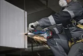 Seseorang yang mengenakan peralatan keselamatan menggiling balok logam, sehingga menimbulkan percikan api.