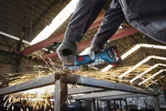 Seseorang yang mengenakan peralatan keselamatan menggiling sinar logam, sehingga menghasilkan percikan terang.