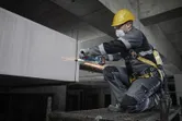 Seseorang yang mengenakan peralatan keselamatan sedang menggiling logam di lokasi konstruksi.