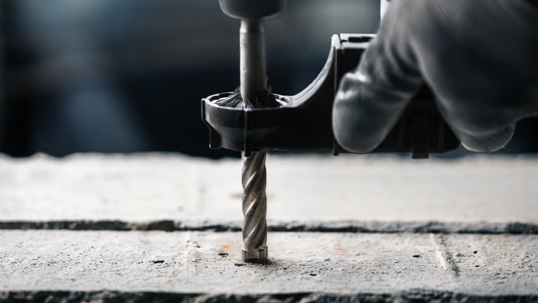 Orang yang mengenakan peralatan keselamatan menggunakan bor untuk membuat lubang di beton.