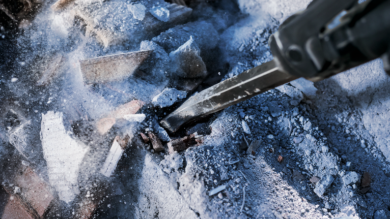 Palu pembongkaran menghancurkan puing-puing beton.