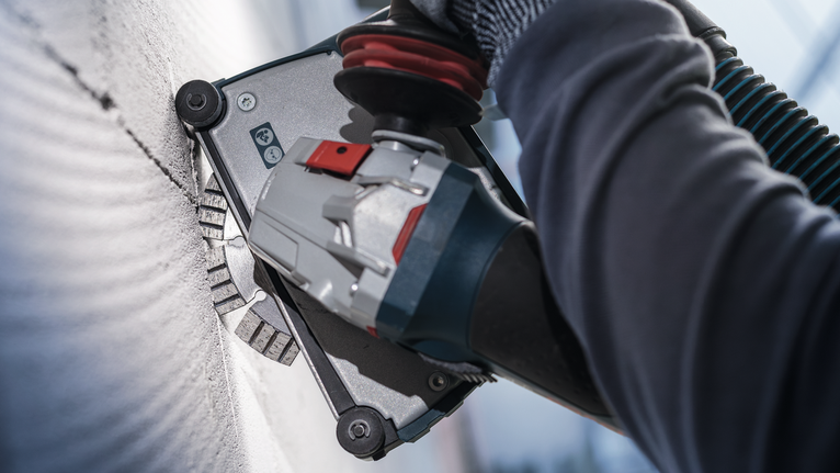 Orang yang mengenakan peralatan keselamatan menggiling tembok dengan perkakas listrik.