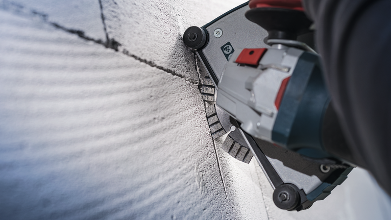 Orang yang mengenakan peralatan keselamatan menggunakan alat listrik untuk memotong alur lurus pada beton.