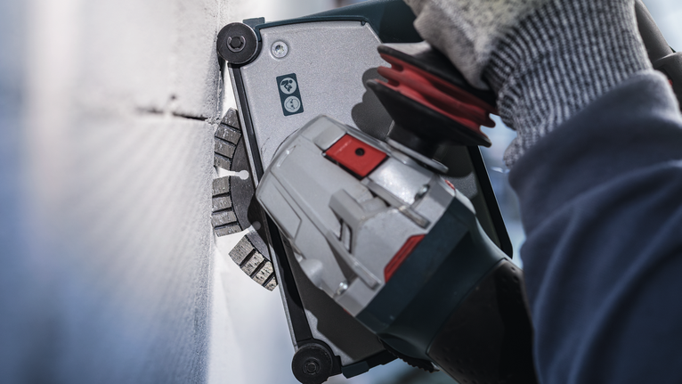 Orang yang mengenakan peralatan keselamatan menggunakan alat listrik untuk memotong dinding.