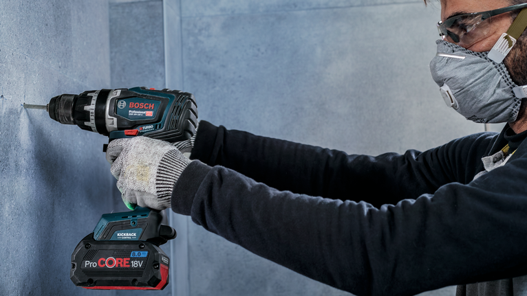 Seseorang yang mengenakan peralatan keselamatan mengebor dinding beton.