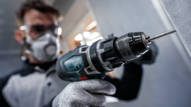 Orang yang mengenakan peralatan keselamatan mengebor dinding dengan alat listrik.