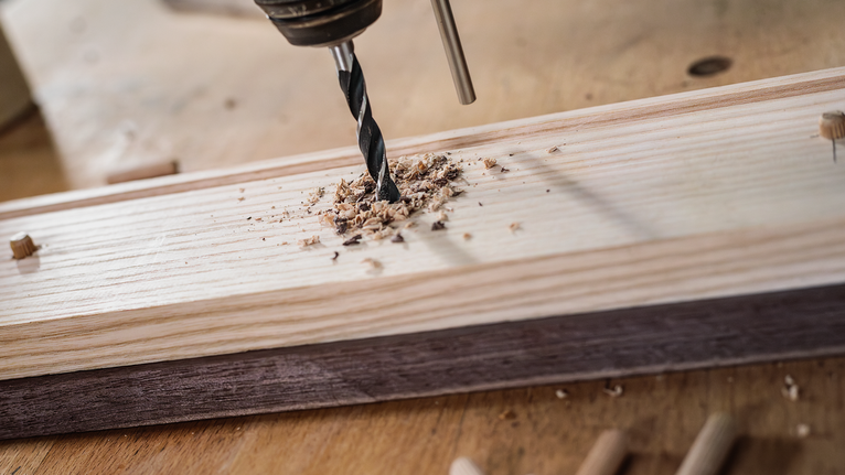 Bor membuat lubang di papan kayu di meja kerja.