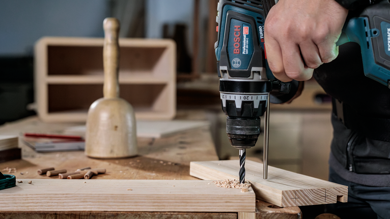 Seseorang mengebor lubang pada papan kayu di bengkel.