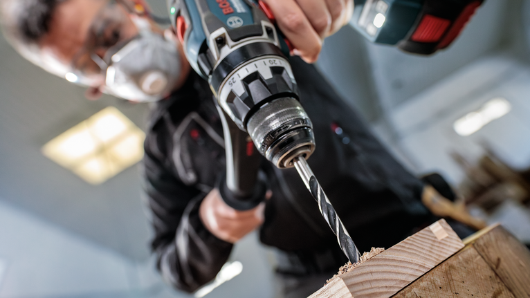 Seseorang yang mengenakan peralatan keselamatan mengebor kayu.