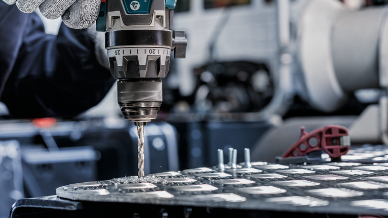 Orang yang mengenakan peralatan keselamatan mengebor lubang pada lembaran logam.