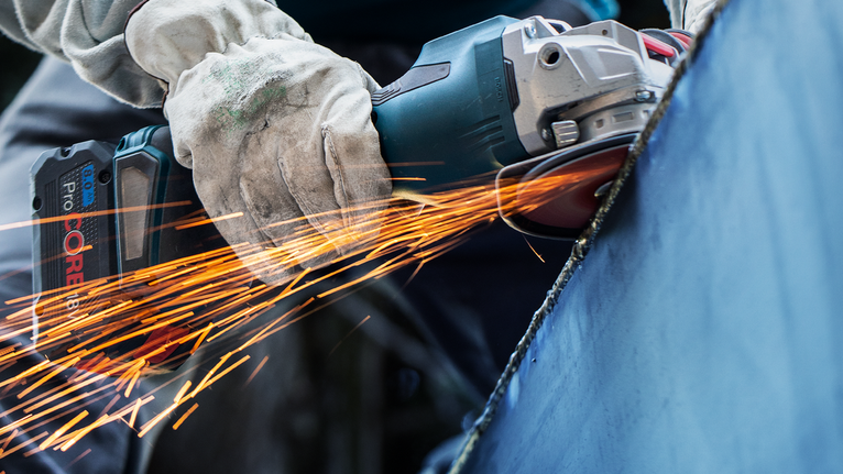 Seseorang yang mengenakan peralatan keselamatan menggiling logam, sehingga menimbulkan percikan api.