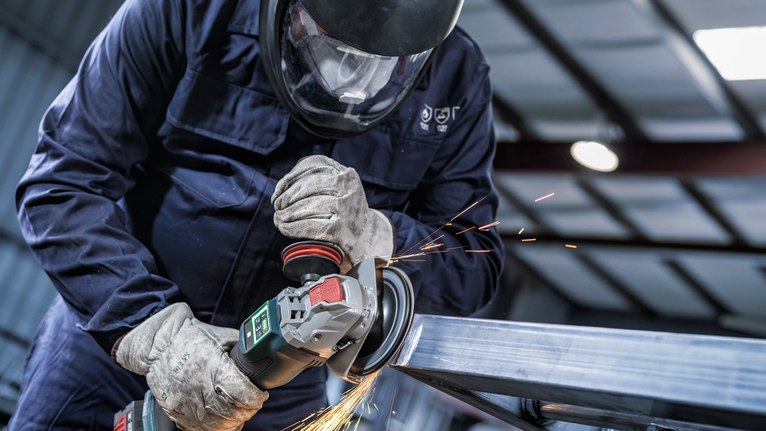 Seseorang yang mengenakan peralatan keselamatan menggiling logam, sehingga menimbulkan percikan api.