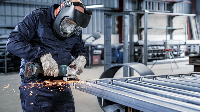 Seseorang yang mengenakan peralatan keselamatan menggiling logam, sehingga menimbulkan percikan api.