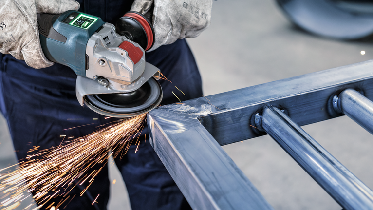 Orang yang mengenakan peralatan keselamatan menggiling logam, menghasilkan percikan terang.