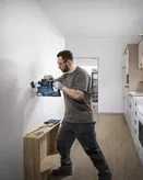 Seseorang yang mengenakan peralatan keselamatan mengebor lubang di dinding dapur.