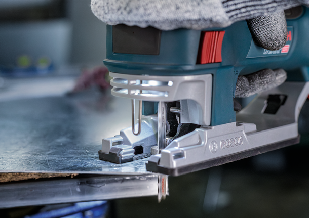 Orang yang mengenakan perlengkapan keselamatan menggunakan gergaji ukir untuk memotong lembaran logam.