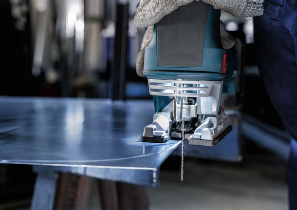 Orang yang mengenakan perlengkapan keselamatan menggunakan gergaji ukir untuk memotong lembaran logam.