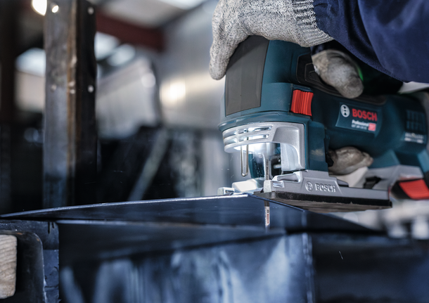 Orang yang mengenakan peralatan keselamatan memotong logam dengan gergaji ukir di lingkungan industri.