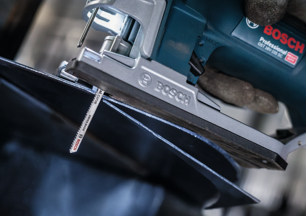 Seseorang yang mengenakan perlengkapan keselamatan menggunakan gergaji ukir untuk memotong lembaran logam.