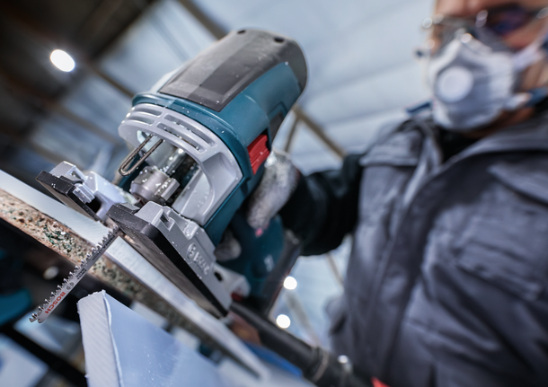 Orang yang mengenakan perlengkapan keselamatan menggunakan gergaji ukir untuk memotong sepotong material.