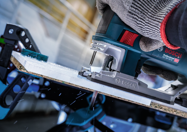 Seseorang yang mengenakan perlengkapan keselamatan menggunakan gergaji ukir untuk memotong selembar kayu.