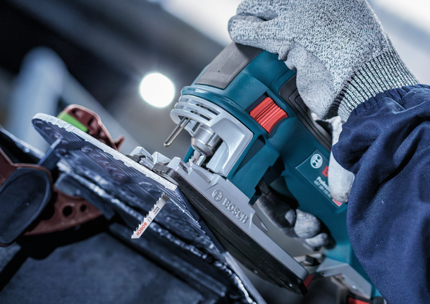 Orang yang mengenakan perlengkapan keselamatan menggunakan gergaji ukir untuk memotong lembaran bahan.