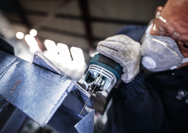 Orang yang mengenakan perlengkapan keselamatan menggunakan gergaji ukir untuk memotong lembaran logam.