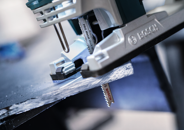 Gergaji ukir memotong lembaran logam gelap di bengkel.