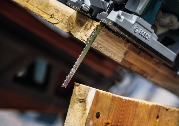 Mata gergaji ukir memotong papan kayu tebal di bengkel.